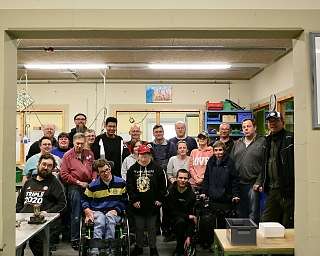 Eine Gruppe von Menschen in einer Werkstatt, lächelnd und zusammen stehend.