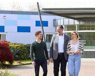 Drei Personen gehen lächelnd vor einem Gebäude.