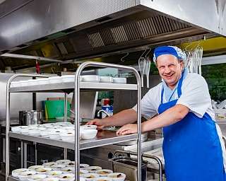 Ein Koch lächelt vor einem Tisch mit Schalen in einer Küche.