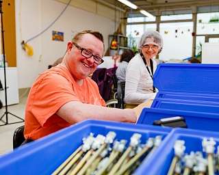 Zwei Personen arbeiten in einer hellen Werkstatt mit blauen Kisten.