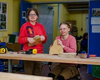Zwei Frauen arbeiten an Holzprojekten in einer Werkstatt.